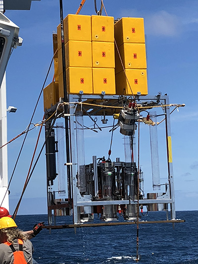 Foto fra det tyske forskningsskib Sonne hvor HADAL-forskere sætter en sediment lander ud. Den kan lave in situ målinger af forskellige parametre nede i de dybe grave. Her er det i Atacama graven ud for Chiles kyst. Landeren  har ballast i spande, som får den til at synke ned på bunden af havet. Når den er færdig med de forprogrammerede analyser, udløses  ballasten akustisk fra skibet,  og de store gule klodser, som er opdrift, får den til at stige op til overfladen. Her lokaliseres den af skibet og bliver samlet op. Denne lander står ofte og måler i mange timer, og derfor er det umuligt at have en wire forbundet til den (tekst og foto: Anni Glud, HADAL).